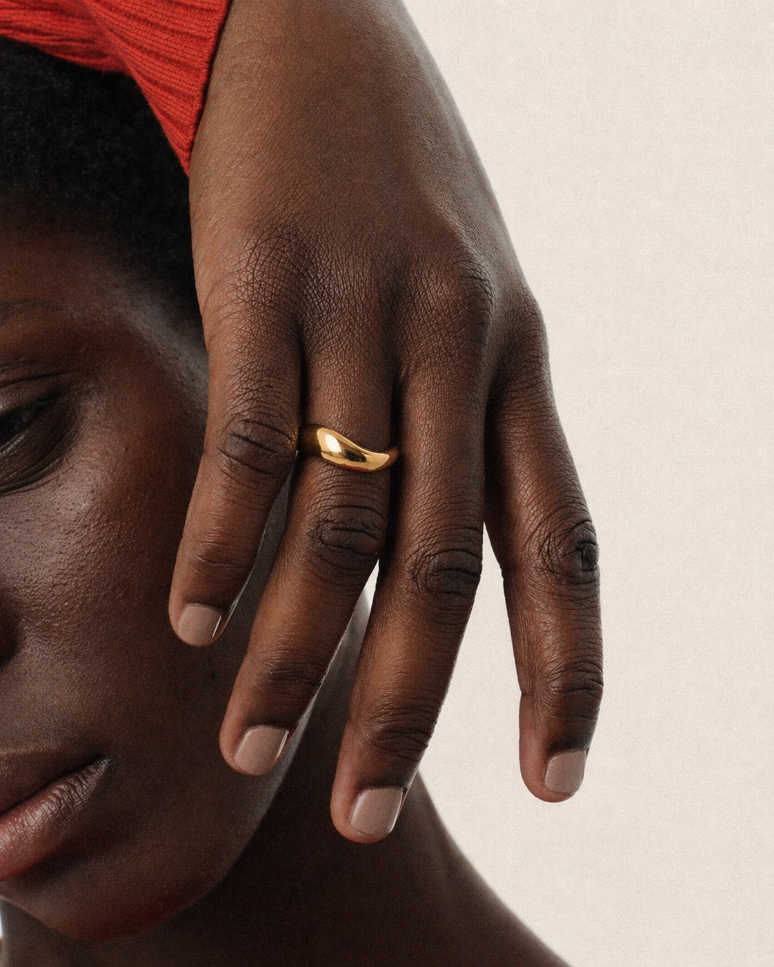 Close-up of a hand with a gold ring on a neutral background