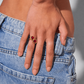Hand wearing a gold ring with red stones against a blurred background