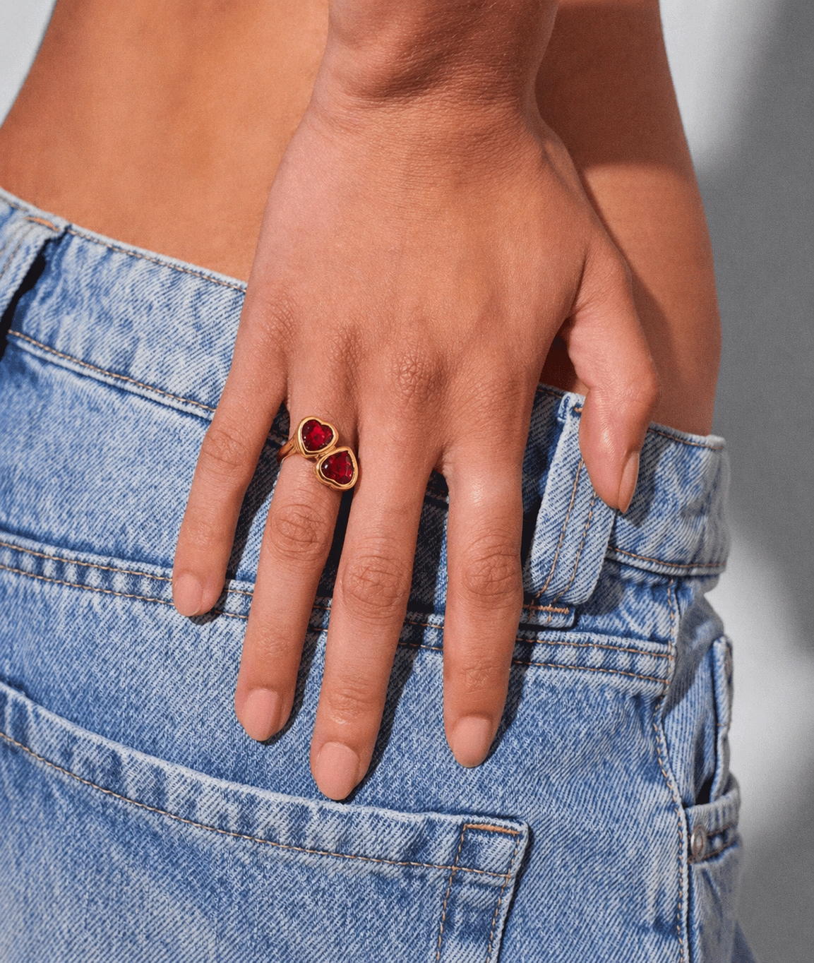 Hand wearing a gold ring with red stones against a blurred background