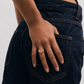 Person wearing dark blue jeans with a gold ring on a plain background