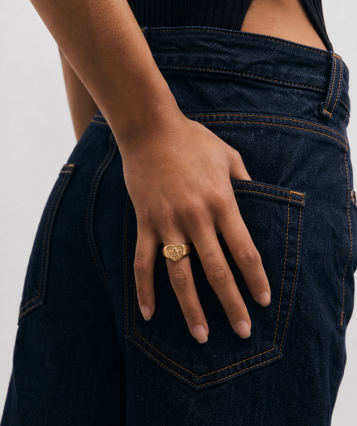 Person wearing dark blue jeans with a gold ring on a plain background