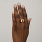 Hand wearing a gold ring on a neutral background