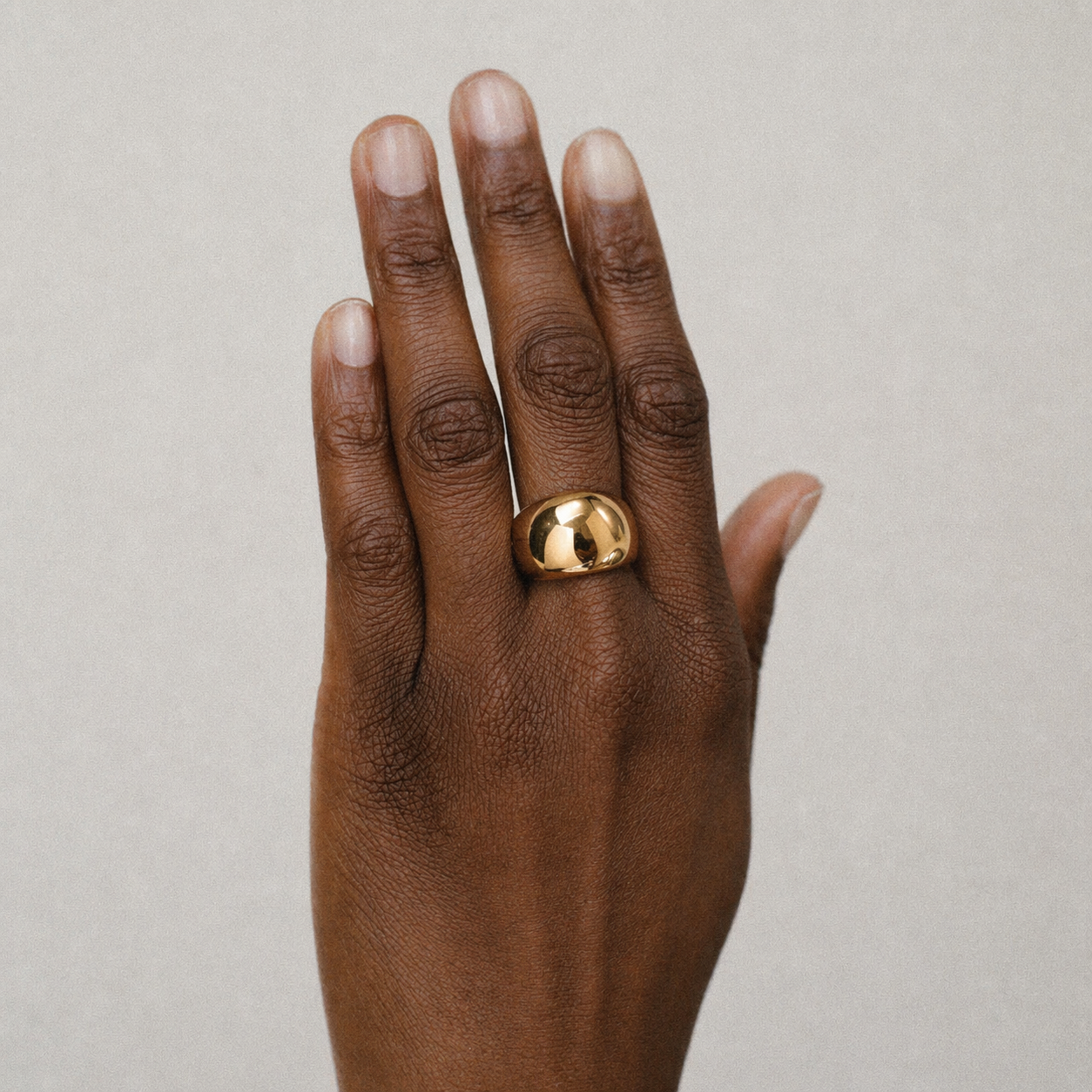 Hand wearing a gold ring on a neutral background