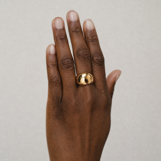 Hand wearing a gold ring on a neutral background