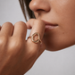 Close-up of a person wearing a gold ring on a neutral background