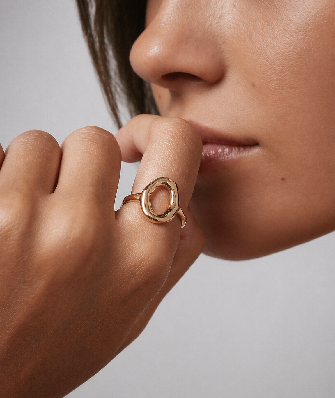 Close-up of a person wearing a gold ring on a neutral background