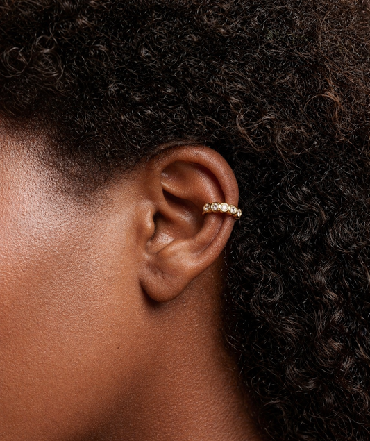 Close-up of an ear wearing a gold earring with a dark background