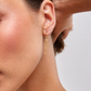 Close-up of a person wearing a gold hoop earring with dangle and with a blurred background