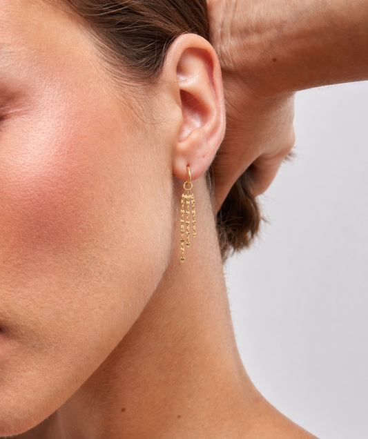 Close-up of a person wearing a gold hoop earring with dangle and with a blurred background
