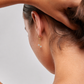 Close-up of a person wearing a gold earring with two small stones on a neutral background