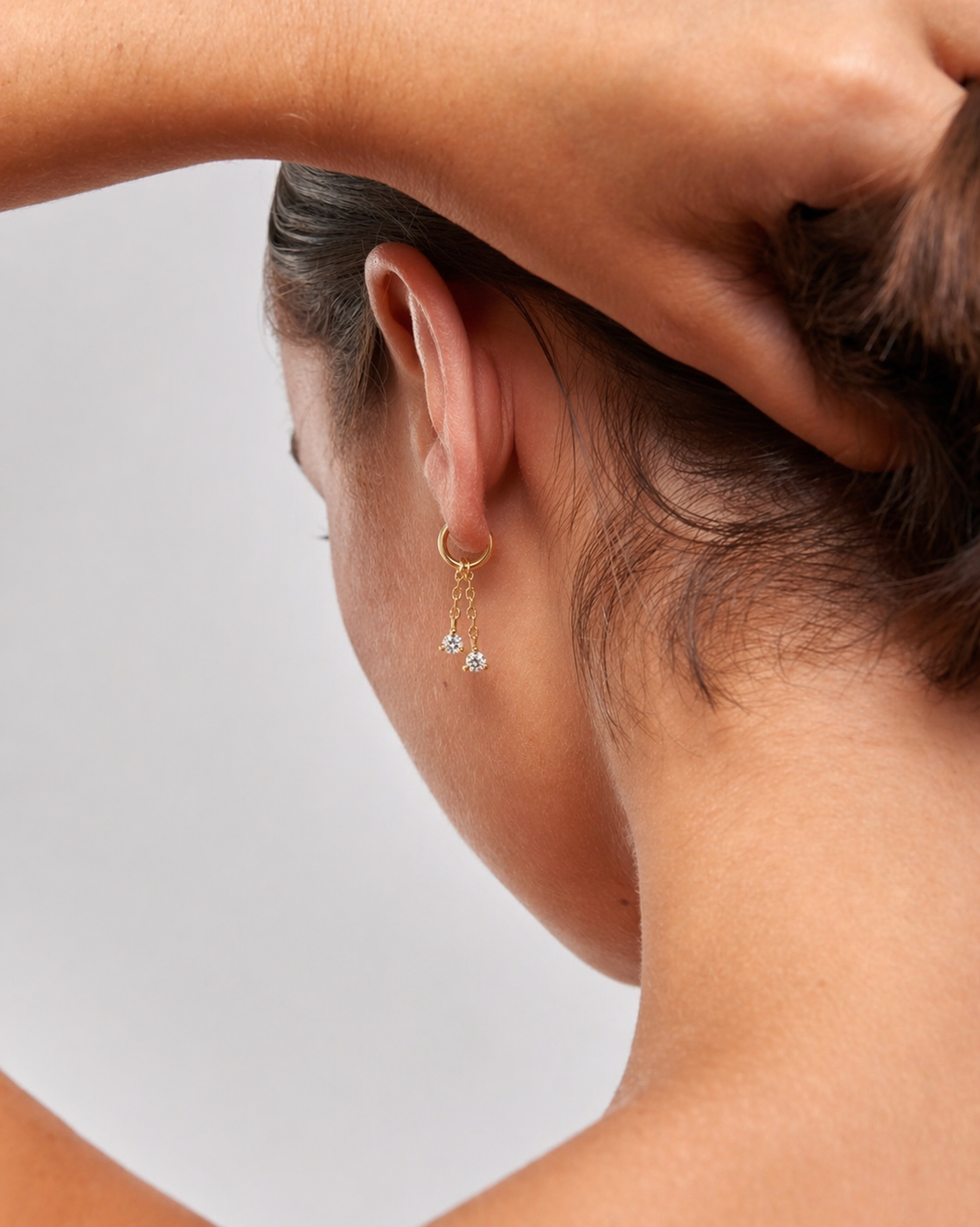 Close-up of a person wearing a gold earring with two small stones on a neutral background