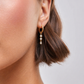 Gold earring with pearls worn by a person on a neutral background