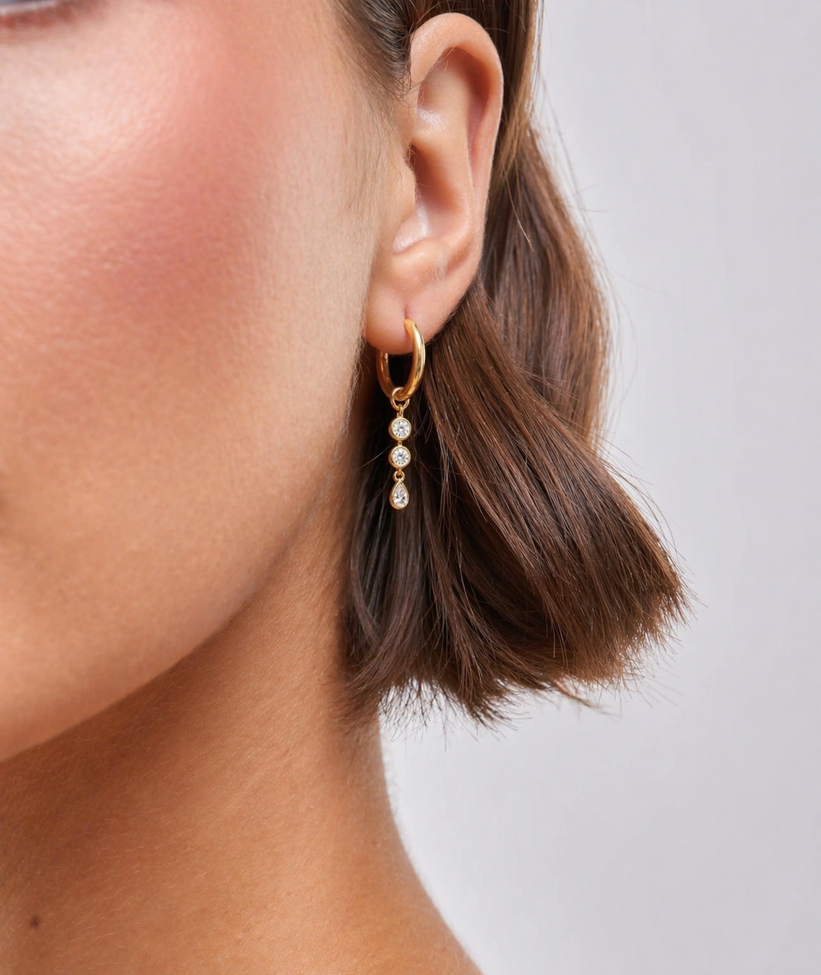 Gold earring with pearls worn by a person on a neutral background