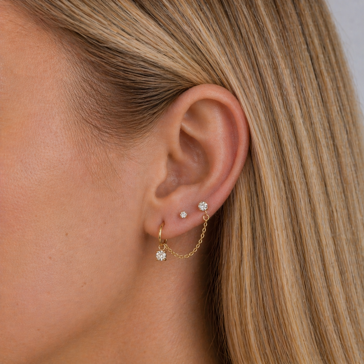 Close-up of an ear wearing gold earrings with small diamonds.