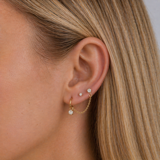 Close-up of an ear wearing gold earrings with small diamonds.