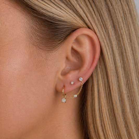 Close-up of an ear wearing gold earrings with small diamonds.