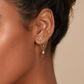 Close-up of an ear wearing gold earrings with clear stones on a neutral background