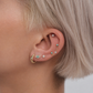 Close-up of an ear with multiple gold and turquoise earrings against a neutral background