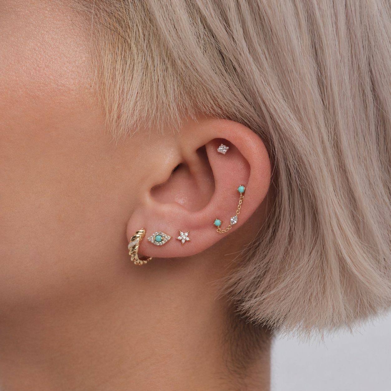 Close-up of an ear with multiple gold and turquoise earrings against a neutral background