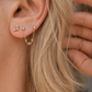Close-up of an ear with gold earrings and a hand adjusting hair.