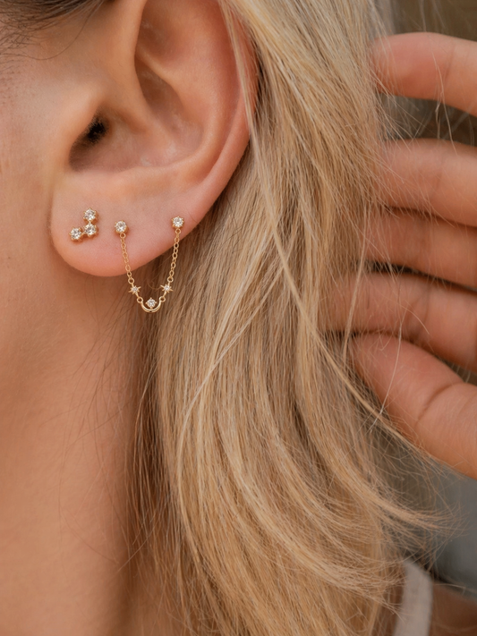 Close-up of an ear with gold earrings and a hand adjusting hair.