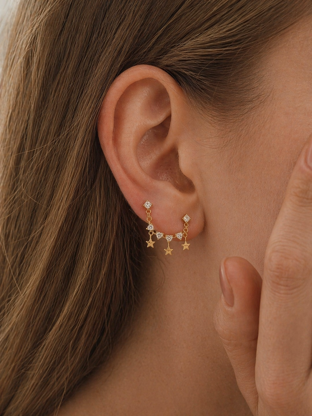 Close-up of an ear wearing gold star-shaped earrings with a blurred background
