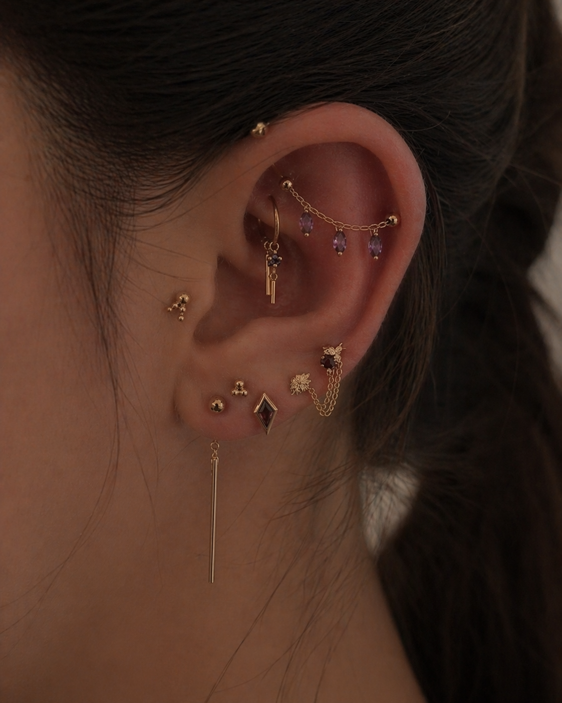 Close-up of an ear with multiple gold earrings against a blurred background