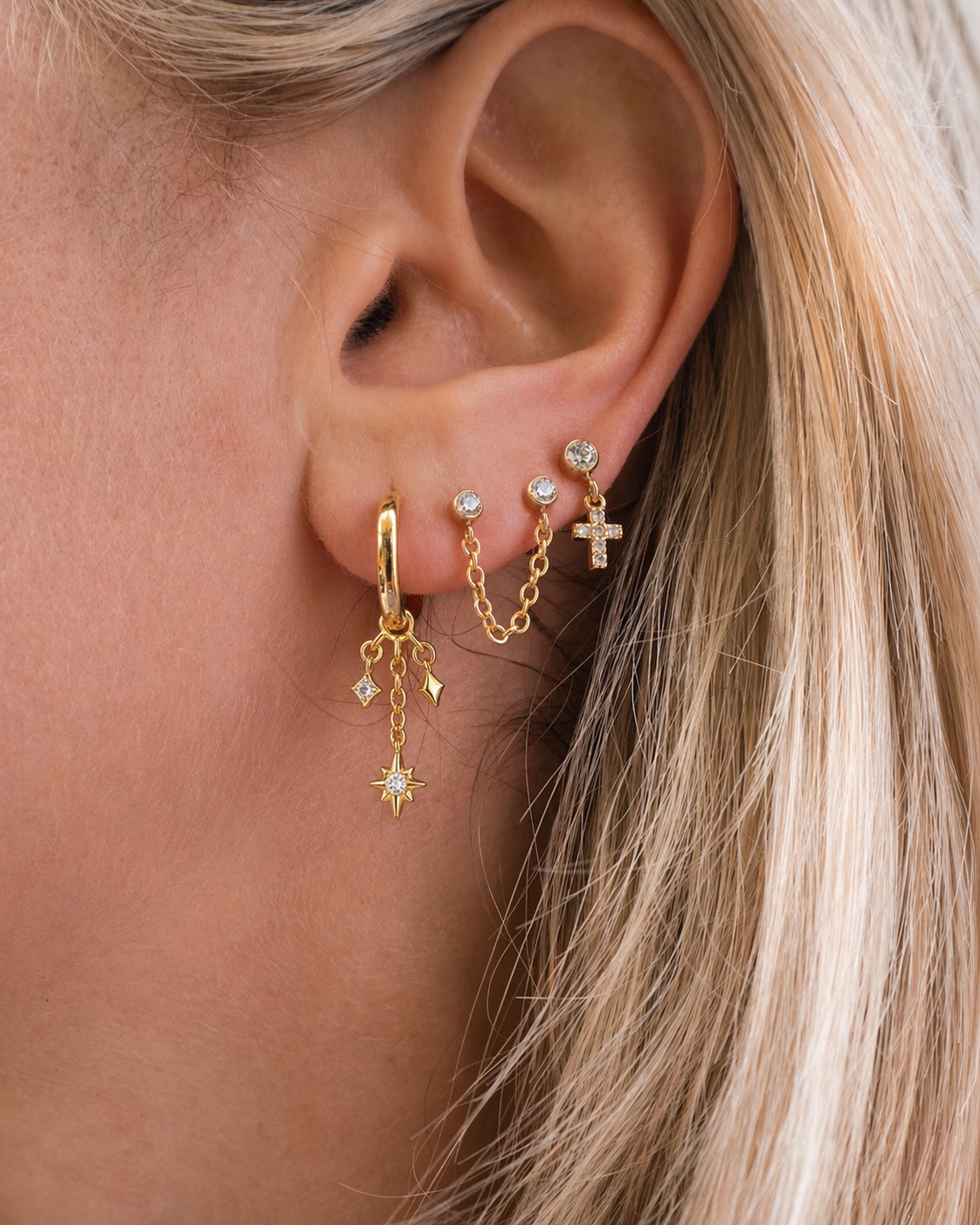Close-up of an ear wearing gold earrings with small charms.