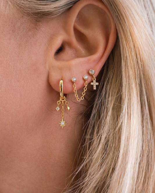 Close-up of an ear wearing gold earrings with small charms.