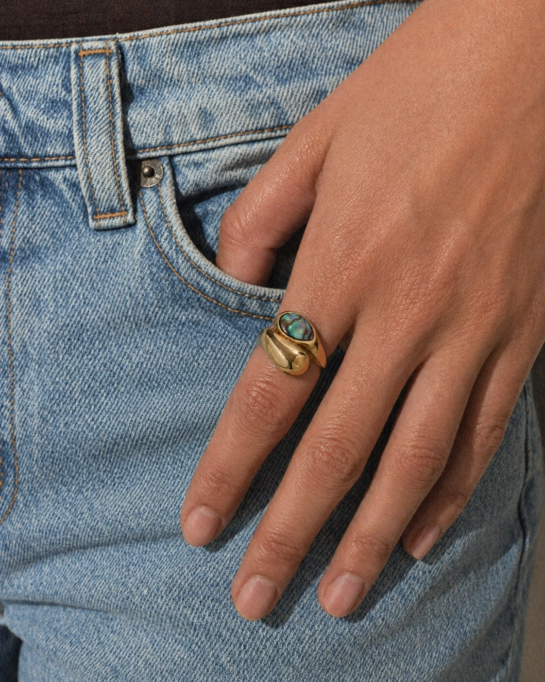 Hand wearing a gold ring with a turquoise stone against a denim background