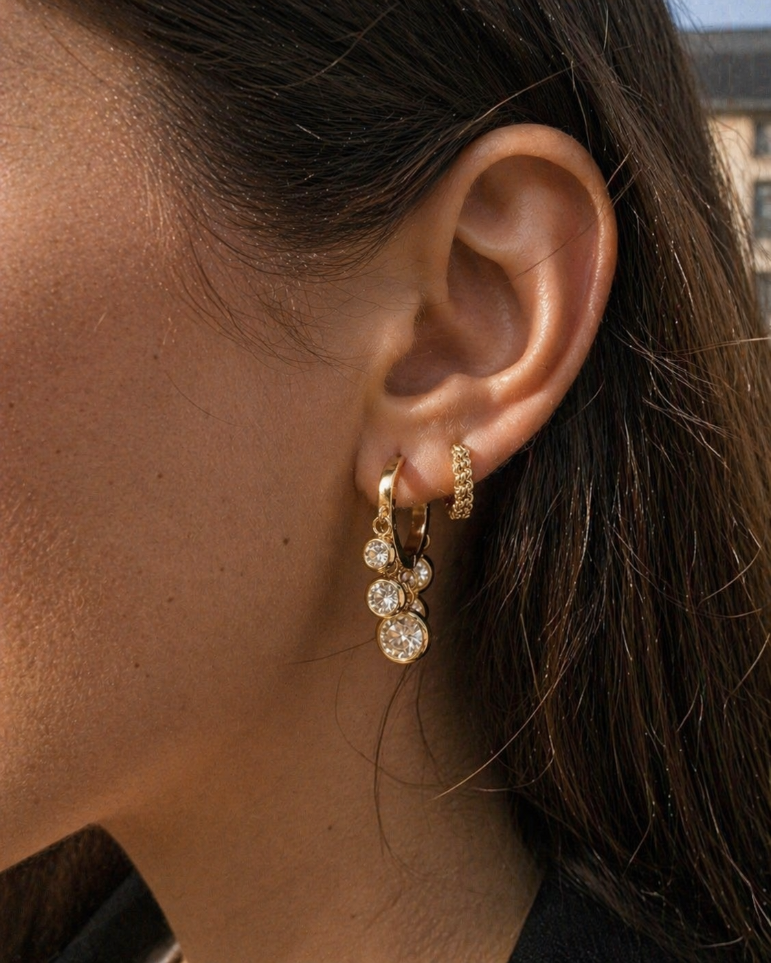 Close-up of an ear wearing gold hoop earrings with small round stones.