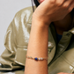 Person wearing a gold bracelet with a blue stone on a neutral background