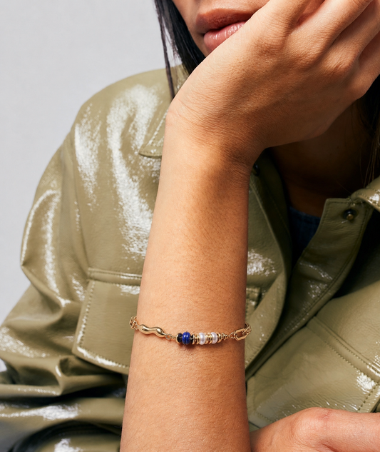 Person wearing a gold bracelet with a blue stone on a neutral background