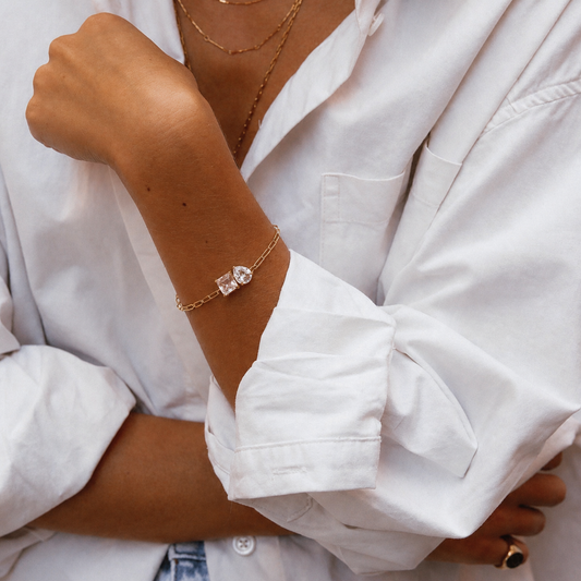 Close-up of a person wearing a gold bracelet with a diamond on a white shirt background