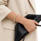 Person holding a black clutch with a pearl bracelet on a neutral background