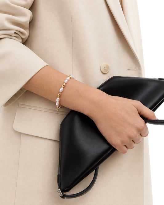 Person holding a black clutch with a pearl bracelet on a neutral background