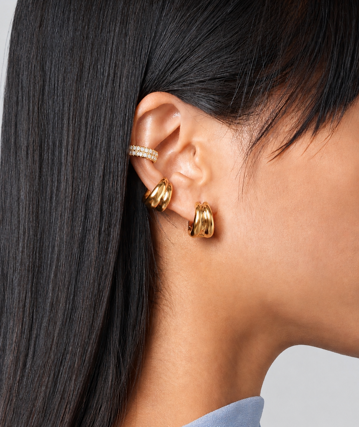 Close-up of an ear wearing gold hoop earrings with a neutral background