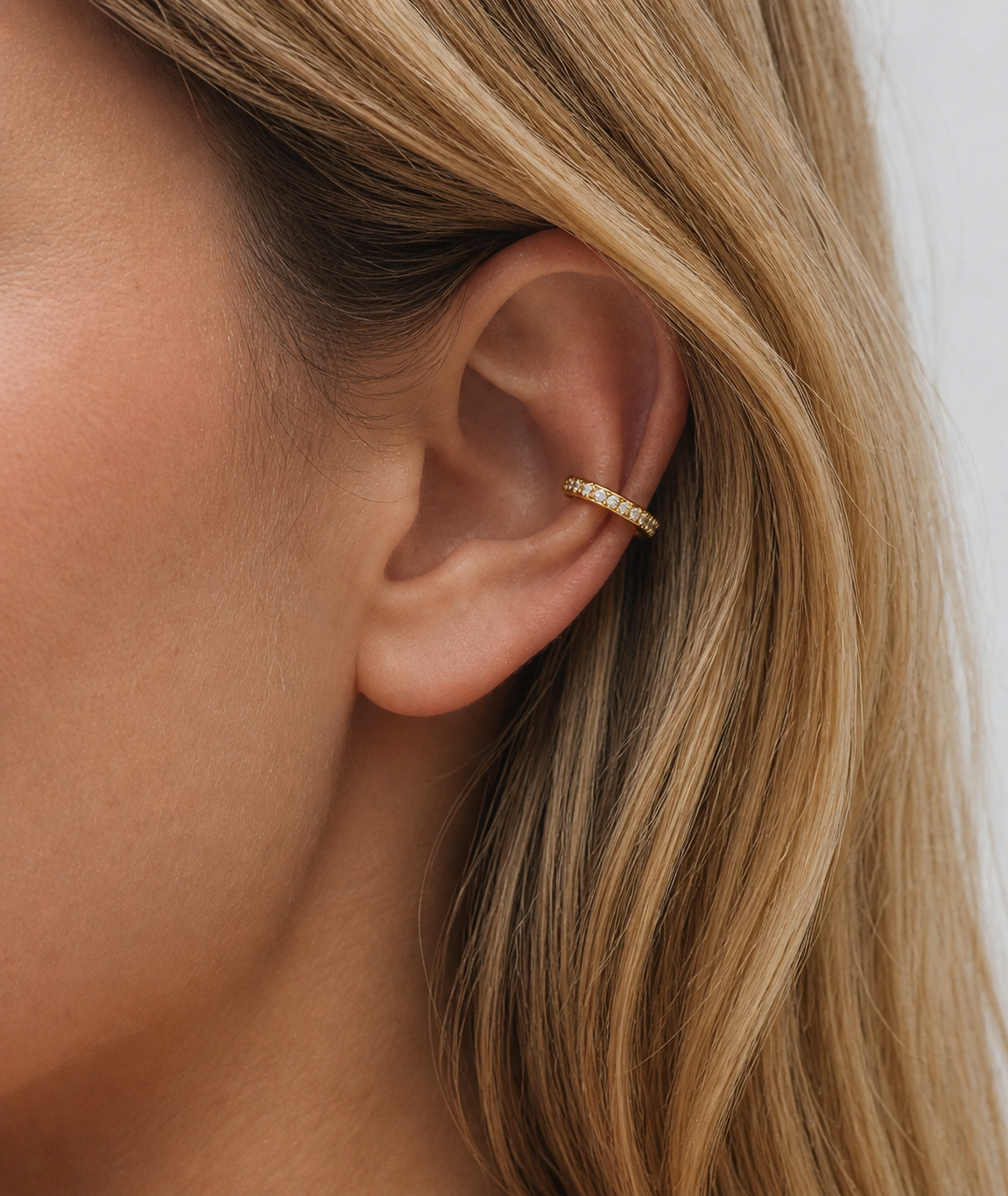 Close-up of an ear wearing a gold hoop earring with blonde hair.