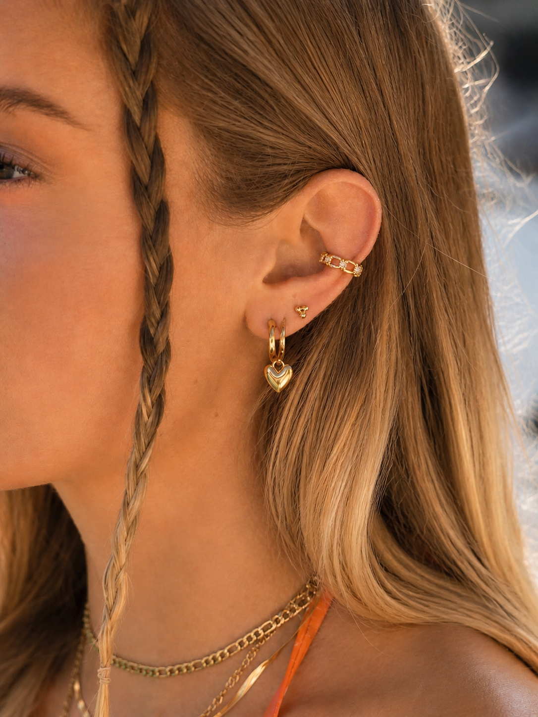 Close-up of a person wearing gold earrings and necklaces with a blurred background