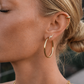 Close-up of a woman's ear wearing gold hoop earrings and a gold earring.