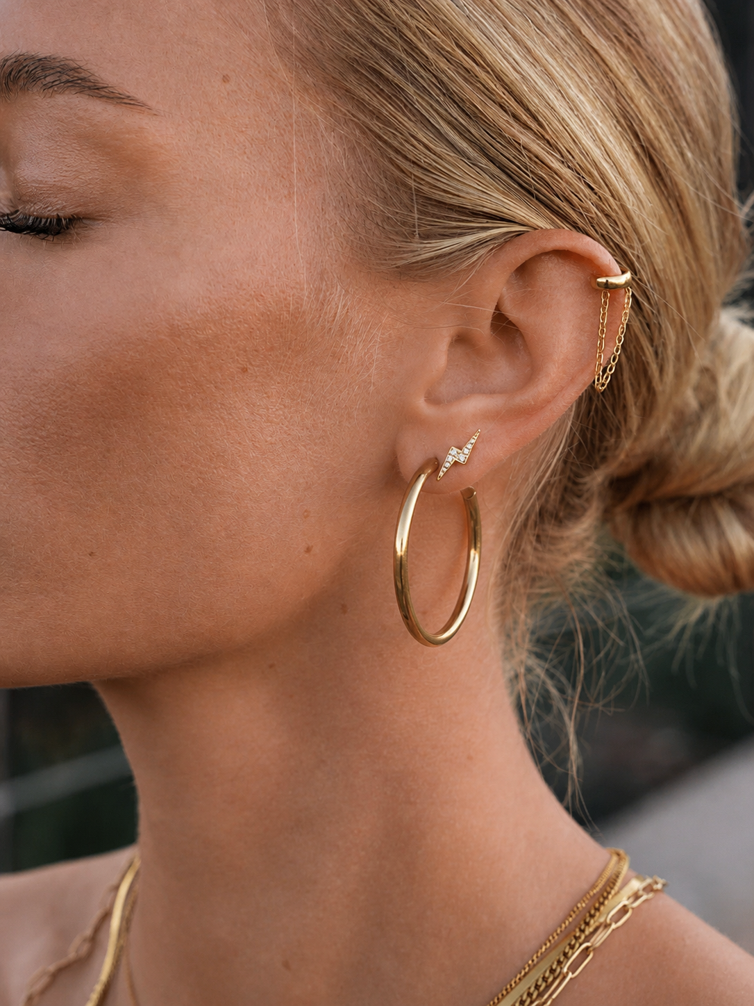Close-up of a woman's ear wearing gold hoop earrings and a gold earring.