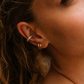Close-up of a woman's ear wearing gold hoop earrings and a diamond ring.