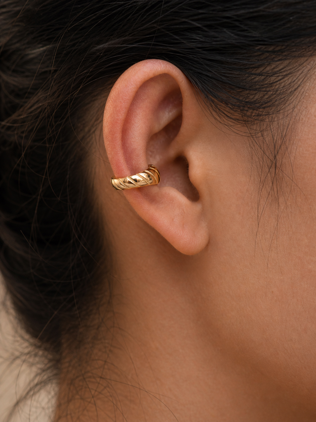 Close-up of an ear wearing a gold hoop earring with blurred hair and skin in the background