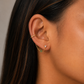 Close-up of an ear with a gold earring and green gemstone on a neutral background