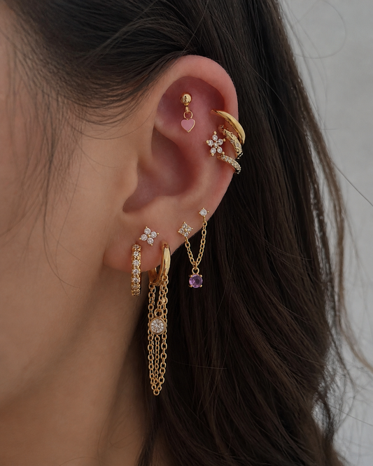 Close-up of an ear with multiple gold earrings on a neutral background