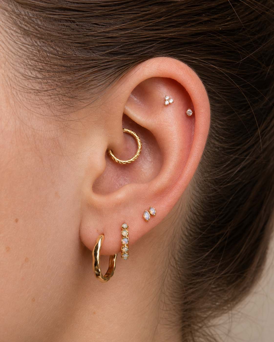 Close-up of an ear with gold hoop earrings and small diamond studs.