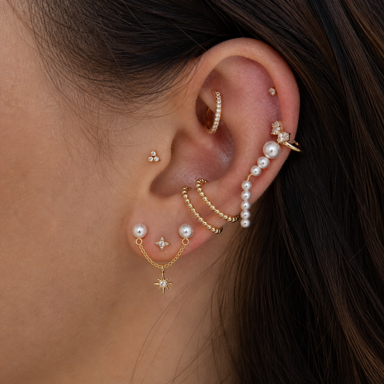 Close-up of an ear with multiple gold and pearl earrings.