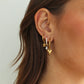 Close-up of an ear wearing gold hoop earrings with floral and heart designs.