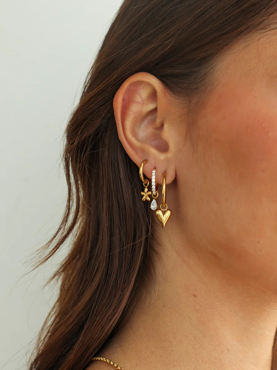 Close-up of an ear wearing gold hoop earrings with floral and heart designs.