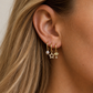 Close-up of an ear wearing gold earrings with pearls and stars, against a neutral background.